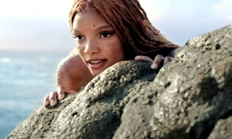 Halle Bailey as Ariel hiding behind a rock in The Little Mermaid