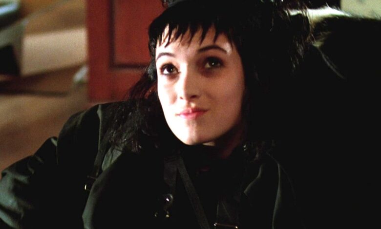Winona Ryder as Lydia Deetz in Beetlejuice sitting in a chair all dressed in black with a pale face and jagged bangs, looking up sort of smugly