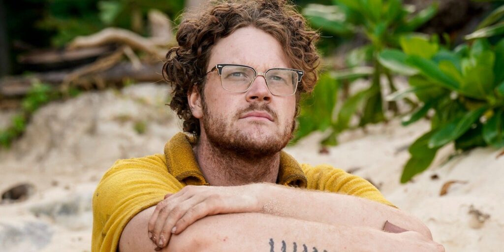 Kane Fritzler Survivor 44 gazing in distance in yellow shirt on beach