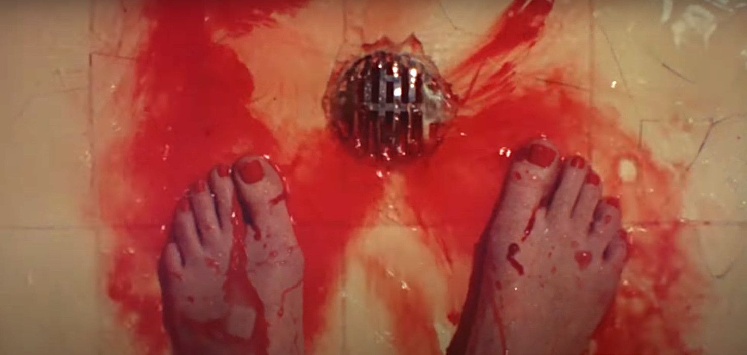 Two bare feet, clearly female, with painted toenails, dripping blood in a shower, while more blood washes down the drain