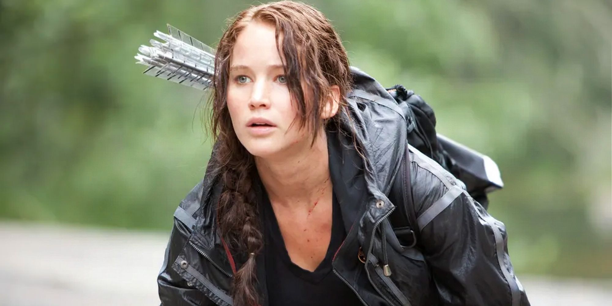 Katniss arrodillada en el suelo, con flechas en la espalda en Los juegos del hambre.