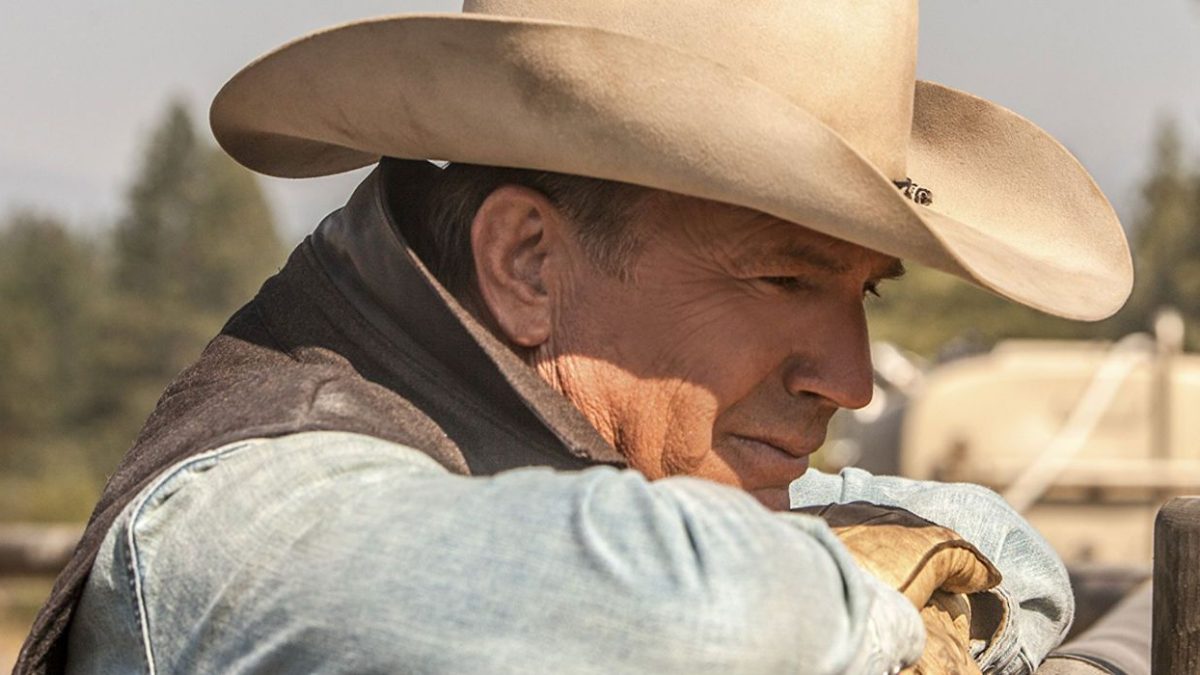 Kevin Costner with his head on top of a ranch fence in Yellowstone
