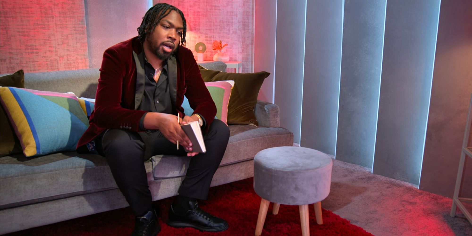 Kenny Love Is Blind temporada 6 sentado en el sofá en vainas inclinado hacia adelante sosteniendo un cuaderno