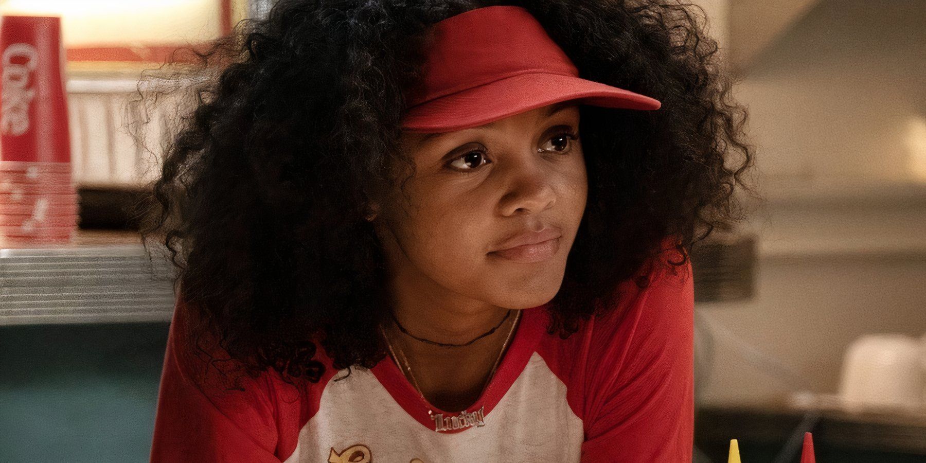 Celeste O'Connor como Lucky Domingo con su uniforme rojo de empleada de hamburguesería y visera en Ghostbusters: Afterlife