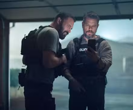 Ben Affleck y Matt Damon con equipo táctico mirando la pantalla de un teléfono en The Rip