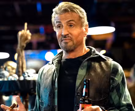 Barney de Sylvester Stallone sosteniendo un cigarro y una cerveza en Expend4bles