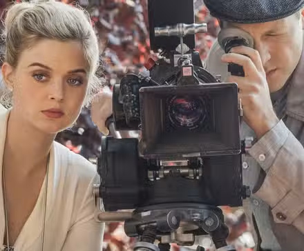 Bella Heathcote como Nicole Dörmer sentada junto a un hombre con una cámara en El hombre en el castillo alto