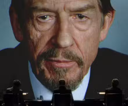 Adam Suttler (John Hurt) hablando desde una gran pantalla de vídeo en V de Vendetta.