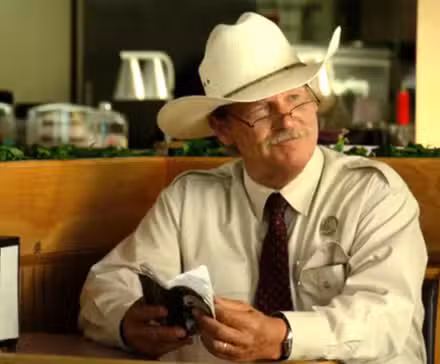 Jeff Bridges como Marcus Hamilton sonriendo y sosteniendo un cuaderno en Hell or High Water