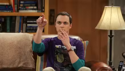 Sheldon sentado en su lugar señalando The Big Bang Theory. 