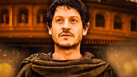 Iwan Rheon luce asombrado en Aquellos a punto de morir con imágenes de la antigua Roma detrás de él.