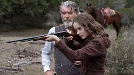 Pierce Brosnan y Sydney Lucas en The Son, con Brosnan detrás de Lucas mientras sostiene una escopeta.