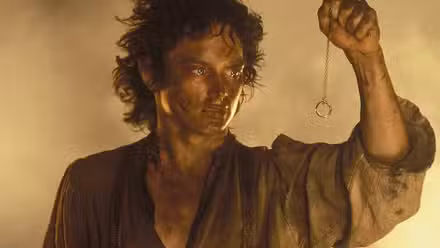 Un Frodo sucio y exhausto sosteniendo el Anillo Único en una cadena frente a él en El Señor de los Anillos: El Retorno del Rey.