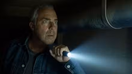 Harry Bosch (Titus Welliver) con una linterna en una alcantarilla y luce preocupado en Bosch: Legacy.