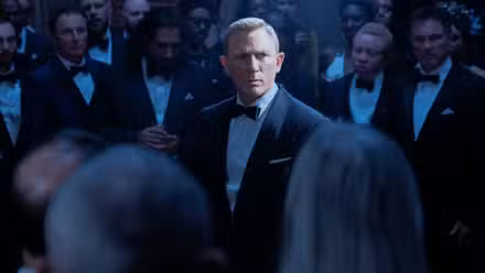 Daniel Craig como James Bond se encuentra en una sala de hombres trajeados.