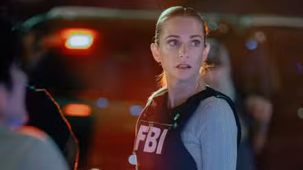 Mentes criminales todavía presenta a AJ Cook como JJ, mirando hacia un lado con su chaleco del FBI y luces de la policía de fondo.