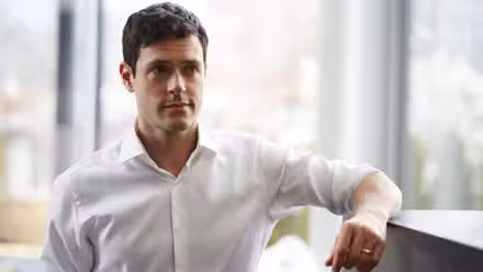 Logan Sanders (Brendan Hines) apoyado en un cubículo en la temporada 4 de Suits