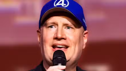 Kevin Feige hablando por un micrófono mientras usa un sombrero de Los Cuatro Fantásticos