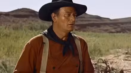 John Wayne como Ethan Edwards a caballo con una pistola en The Searchers