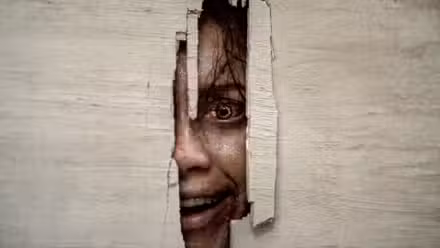 Thya de Luciane Buchanan sonriendo mientras mira a través de un agujero en una puerta en Evil Dead Burn