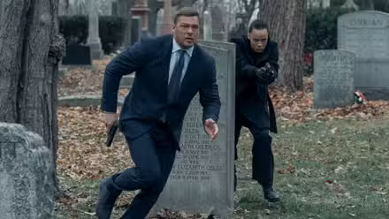 Alan Ritchson como Reacher y Maria Sten como Neagley corriendo en un cementerio.
