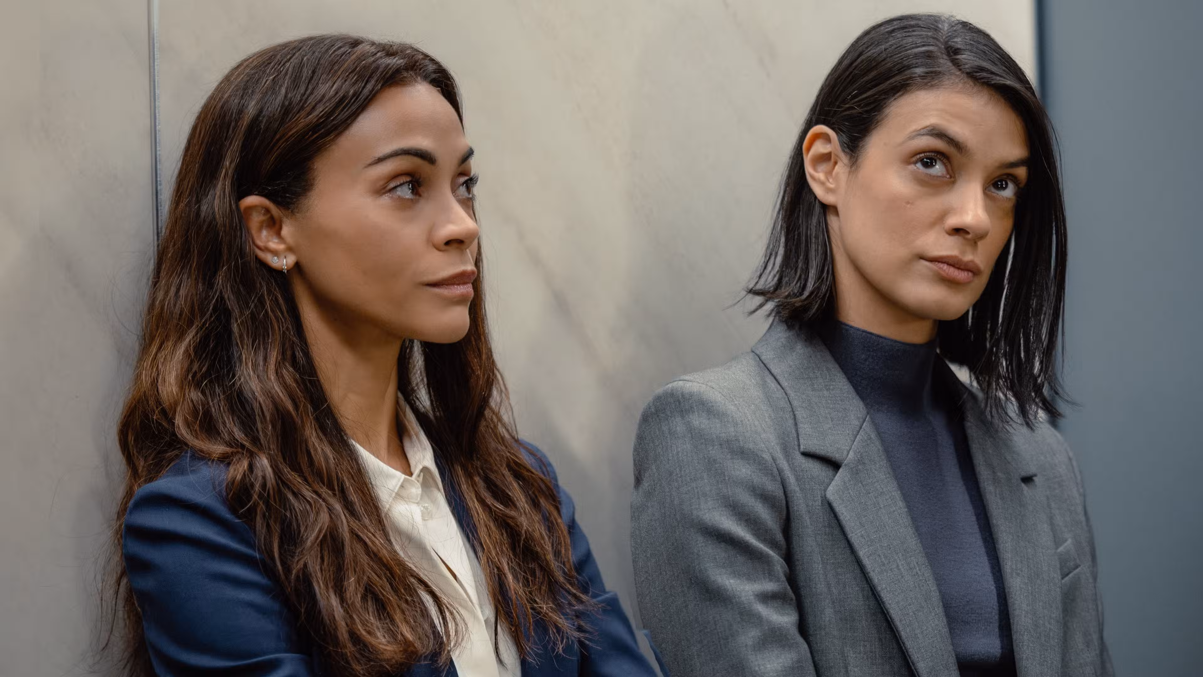 Joe (Zoe Saldaña) y Cruz (Laysla De Oliveira) parados contra la pared en trajes en la temporada 3 de Lioness