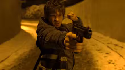Bryan de Austin Abrams apunta con un arma y se mete un dedo en la oreja en Resident Evil