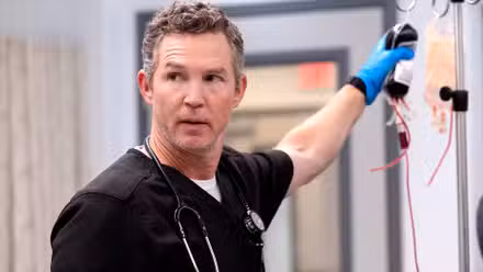 El Dr. Abbot de Shawn Hatosy sosteniendo una bolsa de sangre y mirando hacia la derecha en la temporada 1 de The Pitt