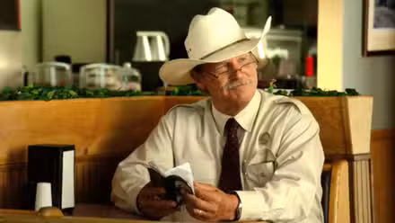 Jeff Bridges como Marcus Hamilton sonriendo y sosteniendo un cuaderno en Hell or High Water