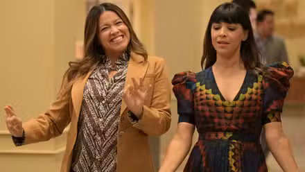 Gina Rodríguez y Hannah Simone caminando por el pasillo de la oficina del periódico en el estreno de la temporada 2.