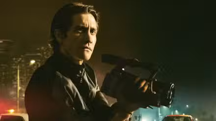 Jake Gyllenhaal sostiene una cámara con la ciudad como telón de fondo en Nightcrawler. 