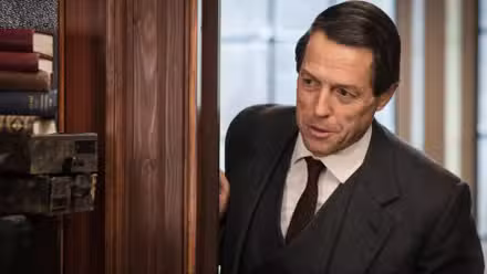 Jeremy Thorpe (Hugh Grant) mirando algo con una sonrisa en su rostro en Un escándalo muy inglés