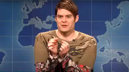 Bill Hader como Stefon en Saturday Night Live luciendo nervioso con el telón de fondo de un mapa mundial