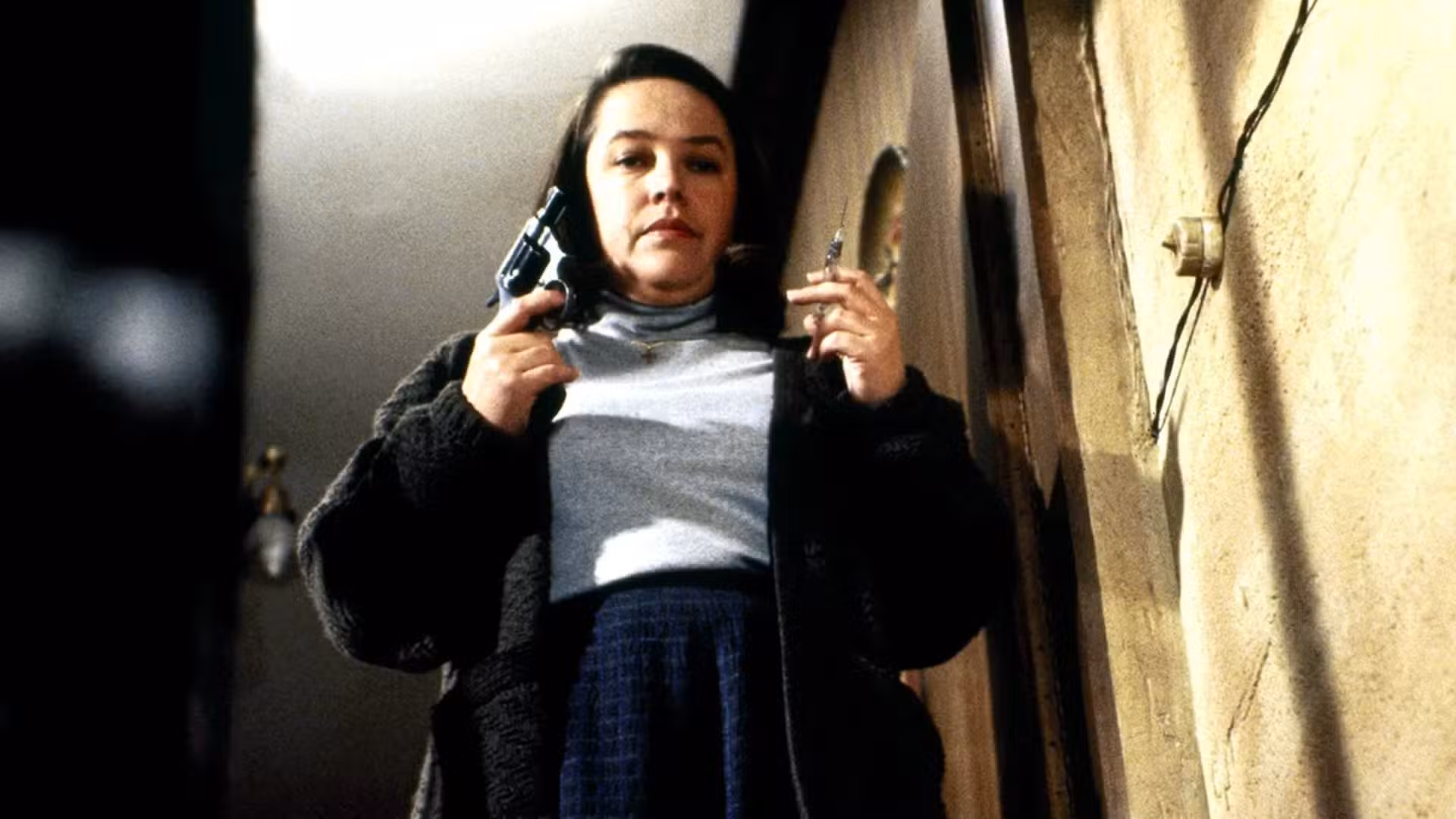Annie (Kathy Bates) se encuentra en lo alto de las escaleras con una pistola y una aguja en Misery.