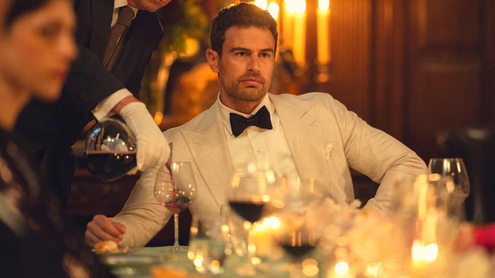 Eddie de Theo James parece enojado mientras alguien le sirve vino en la temporada 2 de The Gentlemen