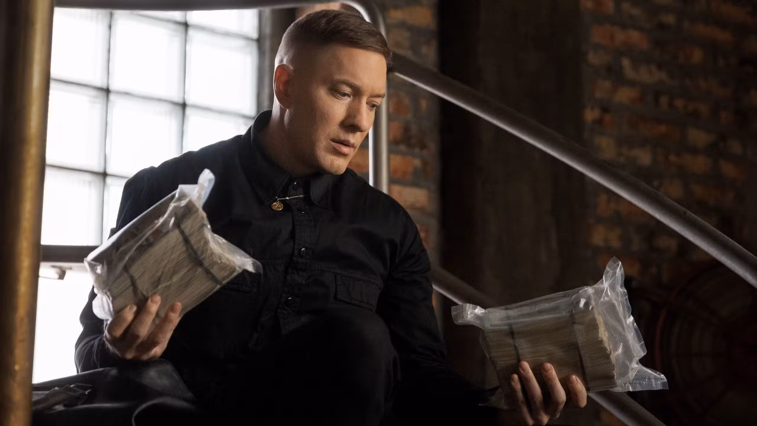 Joseph Sikora como Tommy Egan sosteniendo dos grandes bolsas de dinero en efectivo en Power Book IV: Force.