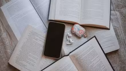 Un teléfono inteligente y airpods apilados encima de una pila de libros abiertos
